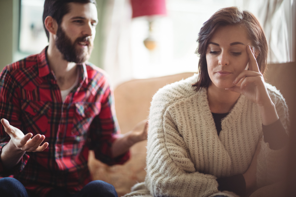 A couple sitting together in emotional tension during a difficult conversation, illustrating the uncomfortable but important emotional challenges that can surface during couples therapy.