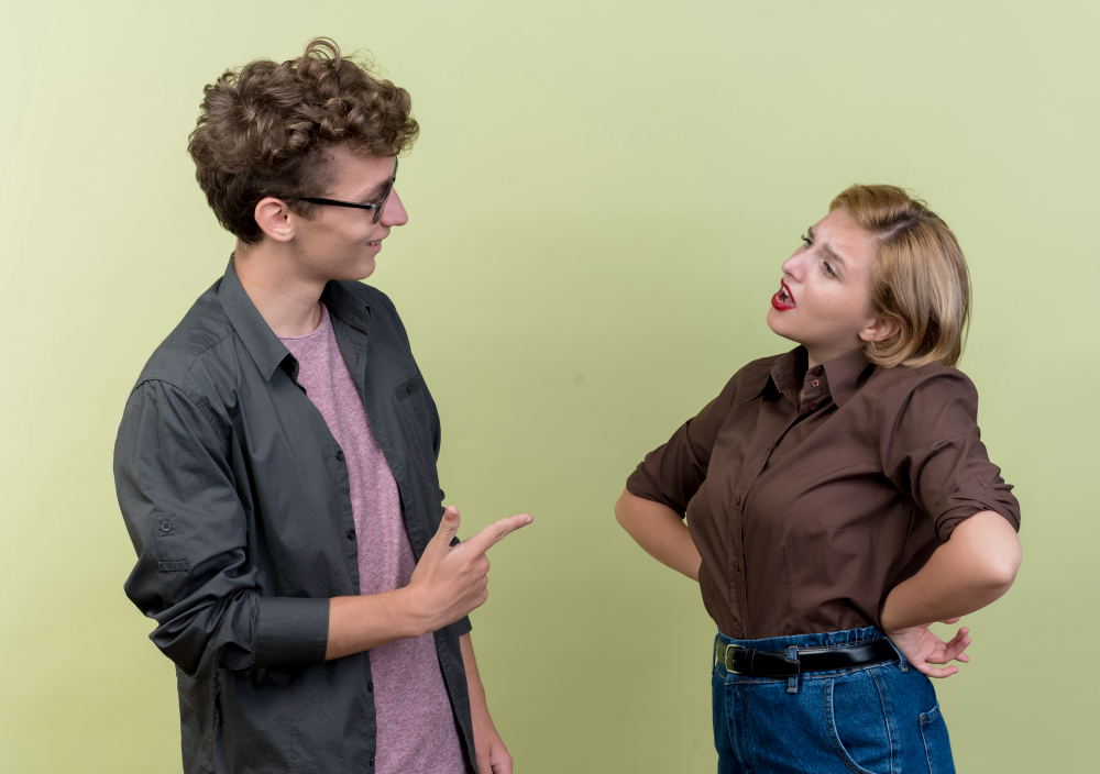 A young man and woman appear to be in a heated conversation, illustrating miscommunication and conflict escalation. The man gestures while speaking, and the woman stands with her hands on her hips, looking frustrated. The image appears beneath the heading ‘Miscommunication and Conflict Escalation.