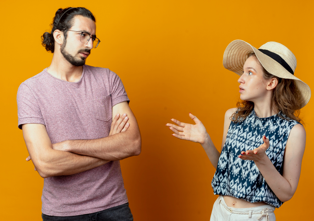 Couple having a tense conversation with defensive body language, illustrating common tone of voice mistakes that can create misunderstanding and relationship conflict.