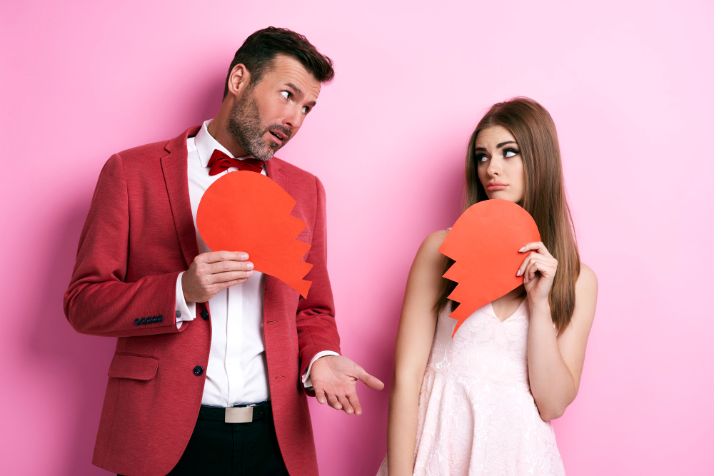 Man and woman holding broken heart symbols, representing contempt in a relationship, communication breakdown, and couples therapy challenges