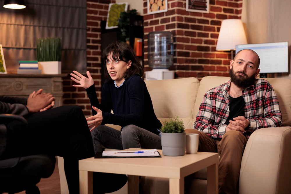 Couple in a therapy session discussing relationship concerns, with one partner actively communicating and the other appearing withdrawn, illustrating the challenges of avoiding difficult conversations in relationships.