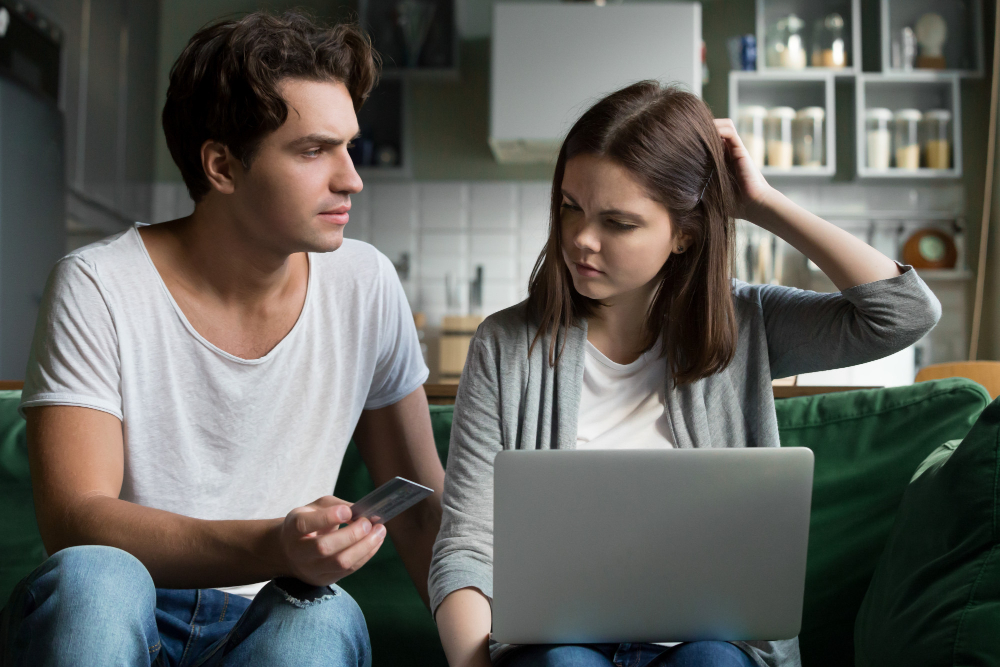 Partner questioning suspicious online activity on a laptop and phone, representing online cheating, cyber infidelity, and relationship trust issues