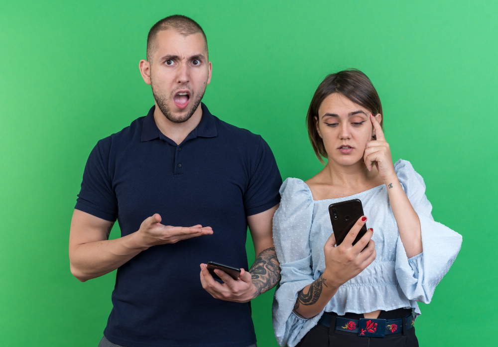 Man reacting with concern while woman looks at her phone, representing emotional disconnection, online boundaries, and common causes of cyber infidelity in relationships.